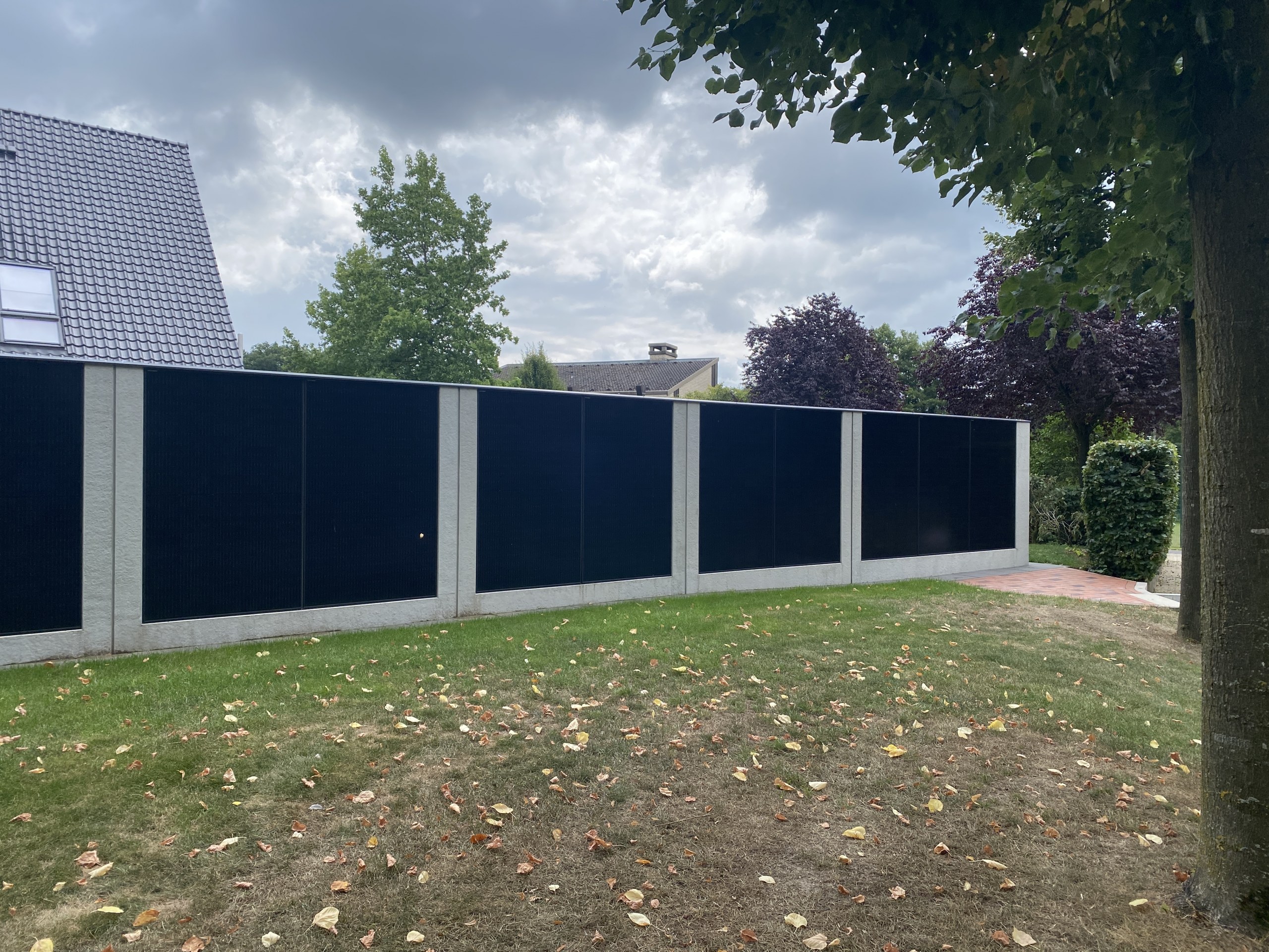 Solarzaun mit schwarzen Solarmodulen in einem privaten Garten vor Wohnhäusern.